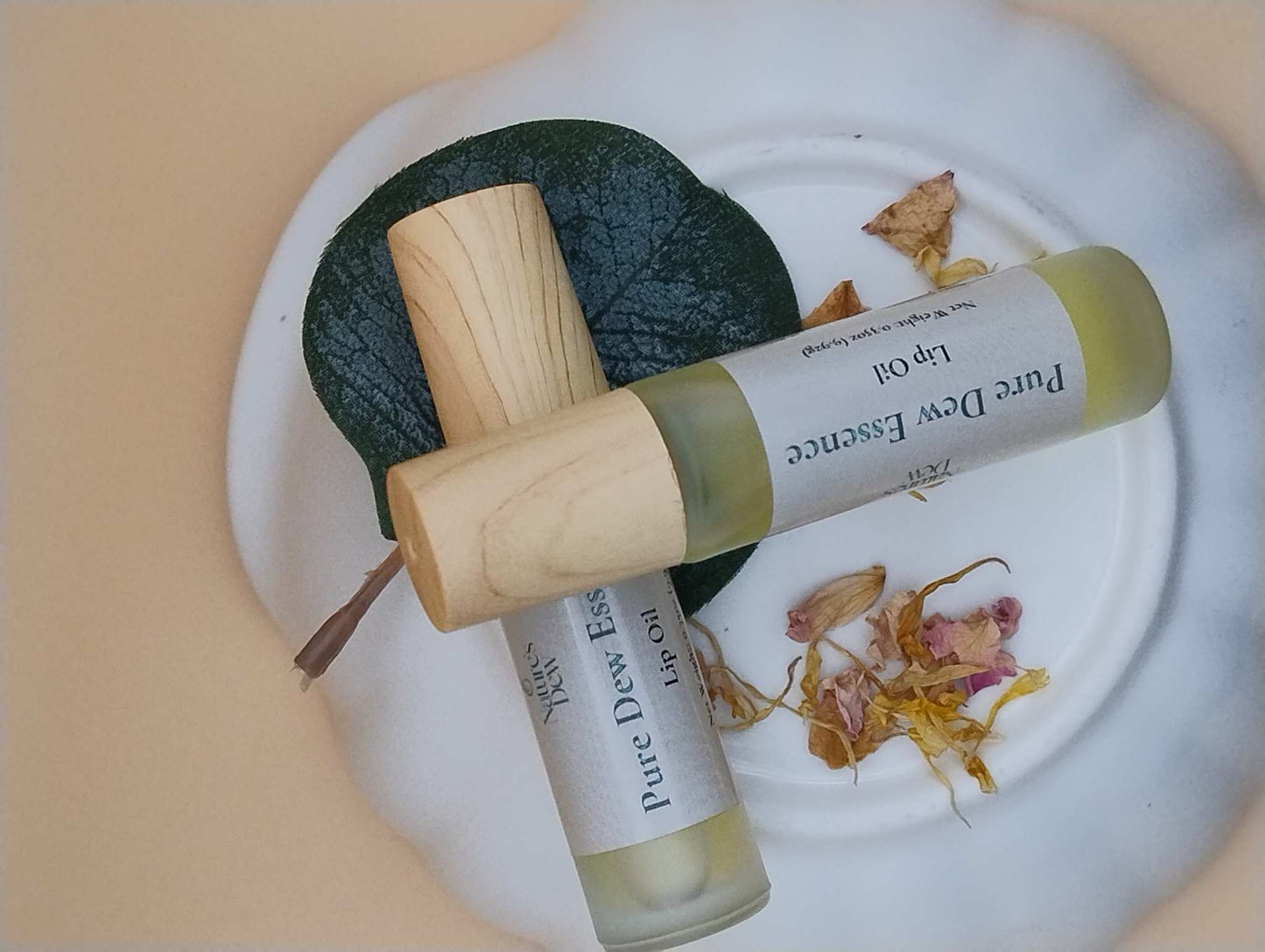 Pure Dew Essence Lip Oil bottles on a decorative plate, surrounded by leaves and petals.