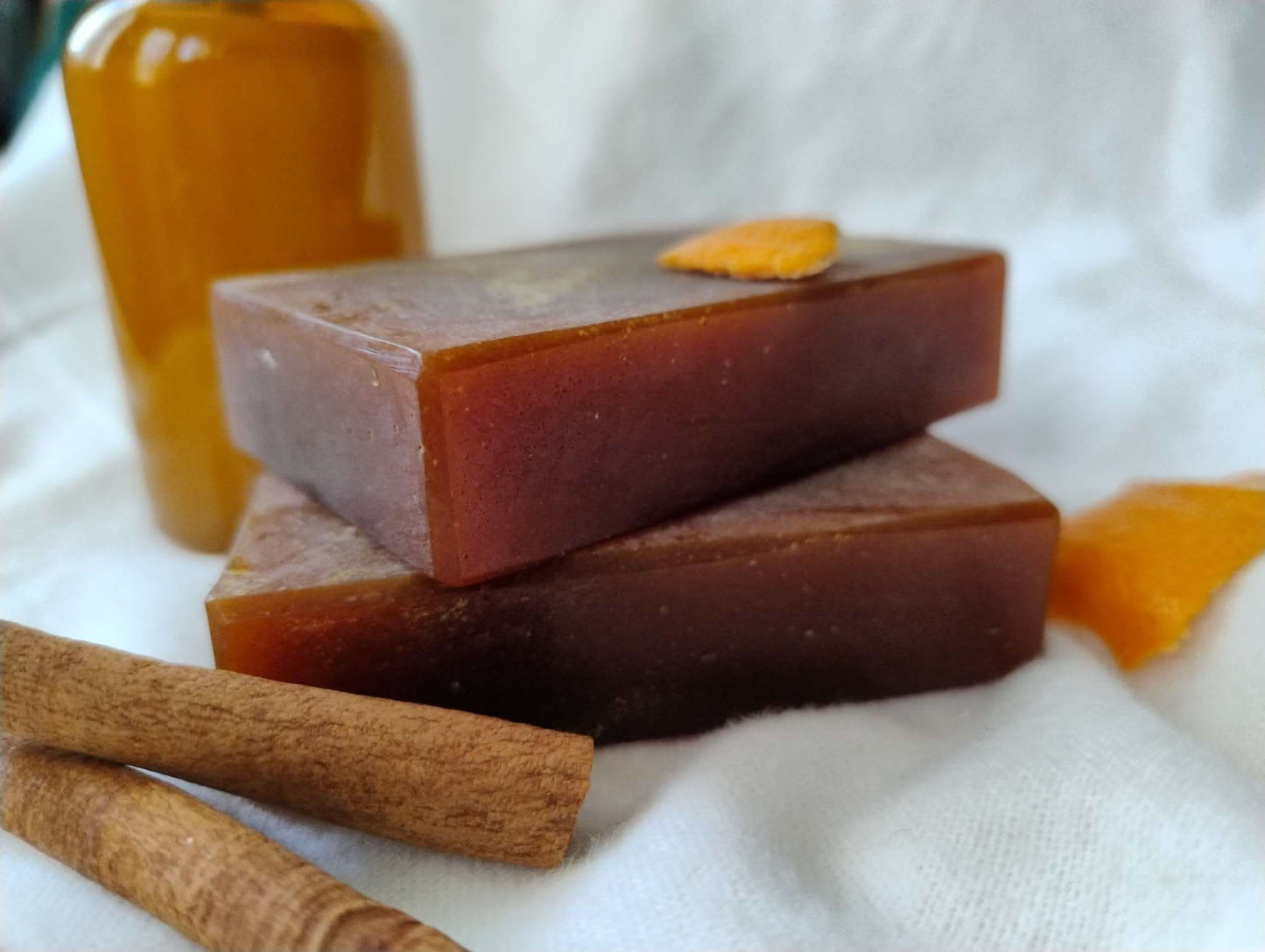 Autumn Ember Ritual Soap bars with warm amber color, cinnamon sticks, and orange peel on white fabric background