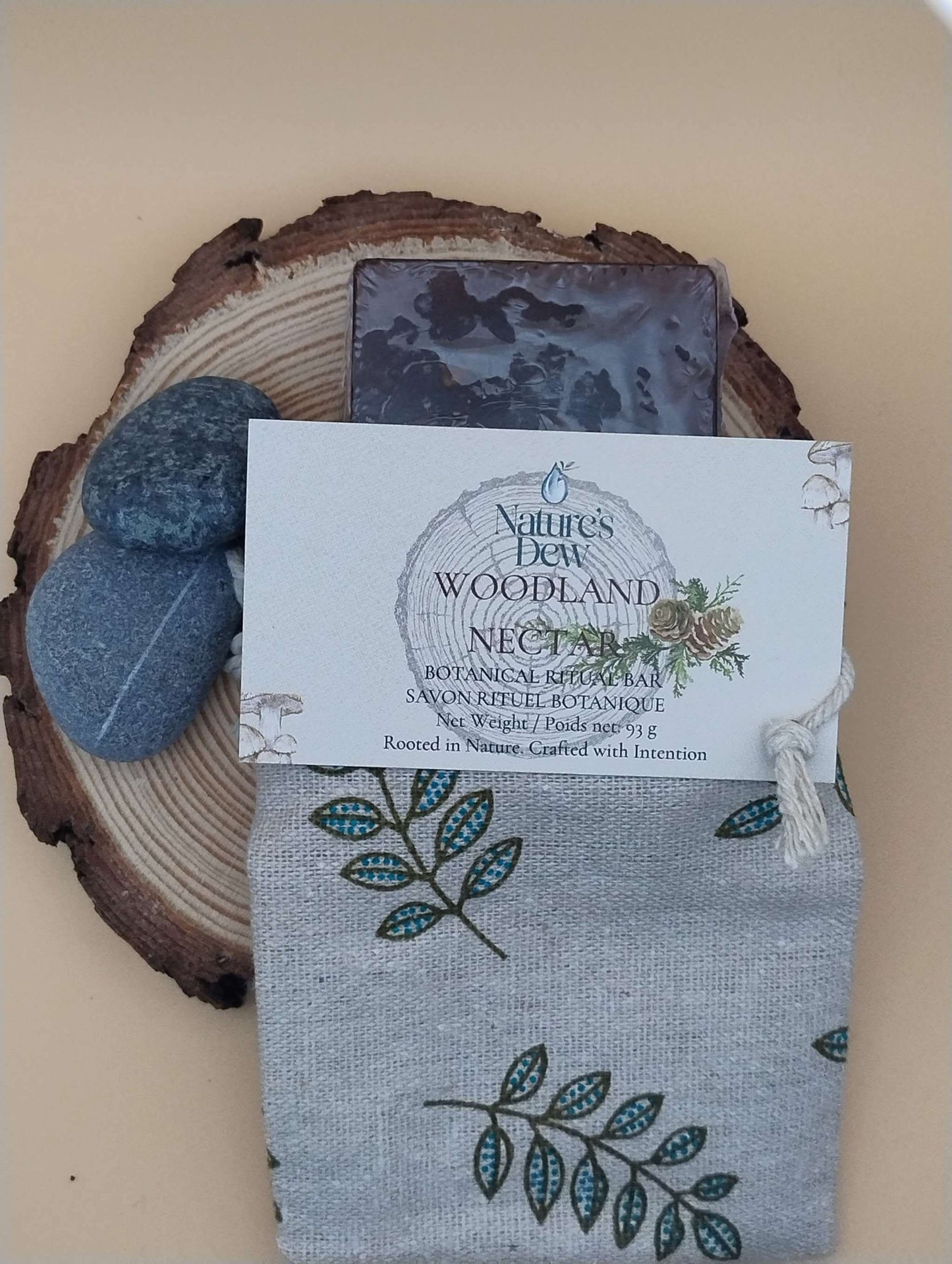 Woodland Nectar Ritual Soap Bar on a wooden slice with decorative stones and a printed fabric pouch.
