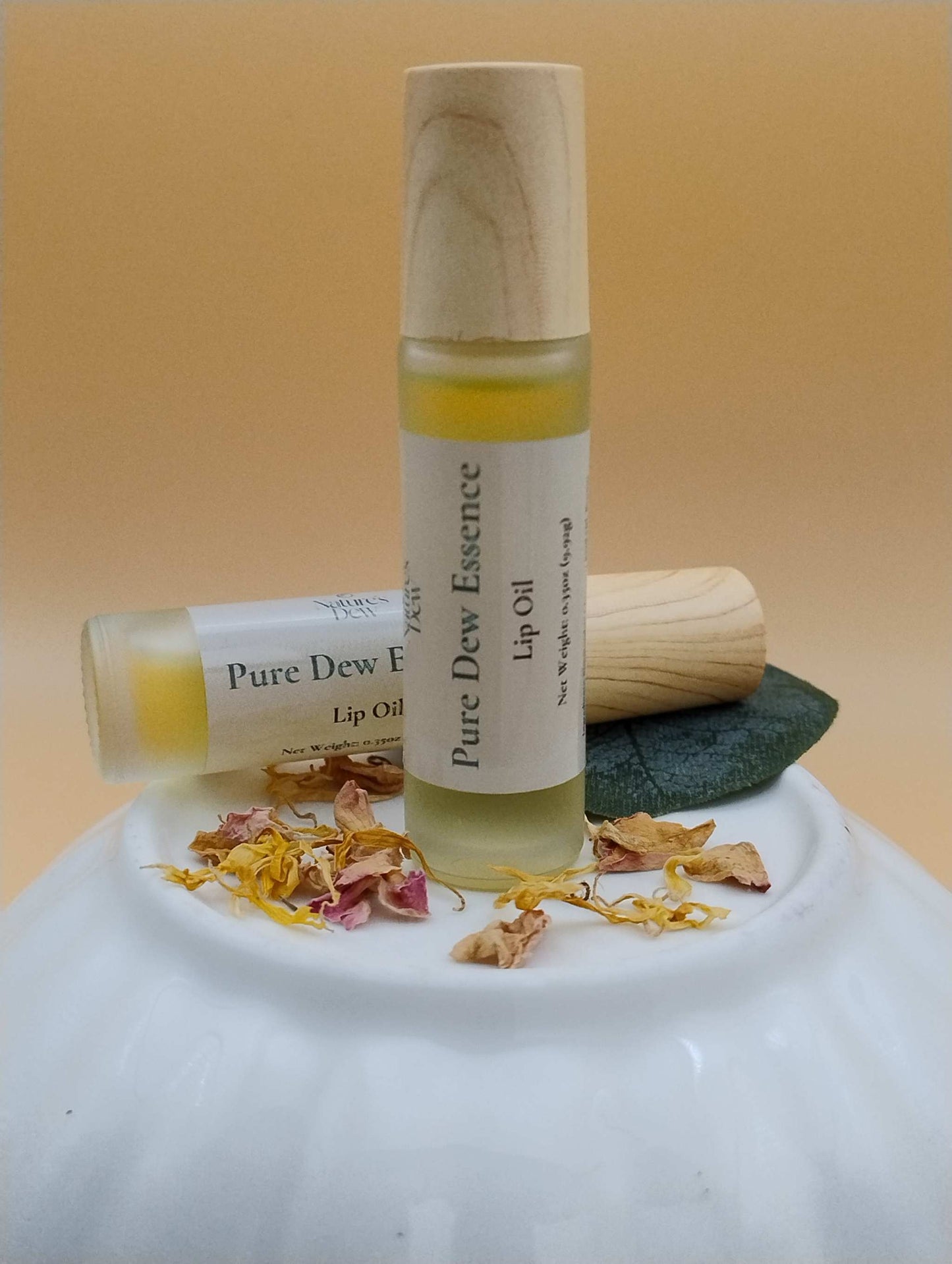 Pure Dew Essence Lip Oil with natural ingredients displayed on white ceramic surface.