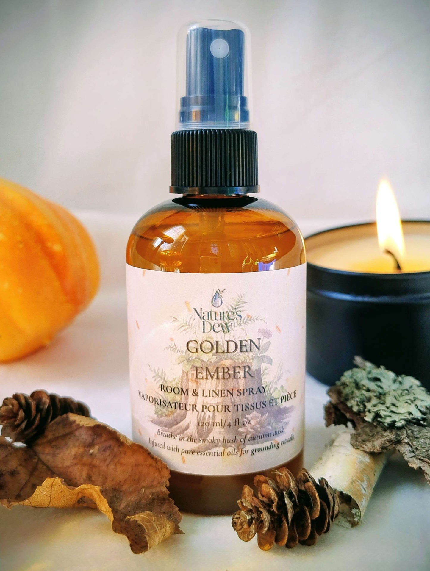 Golden Ember Linen & Room Spray bottle with autumn decor and a lit candle, evoking warm, earthy, smoky cedarwood and vetiver scent