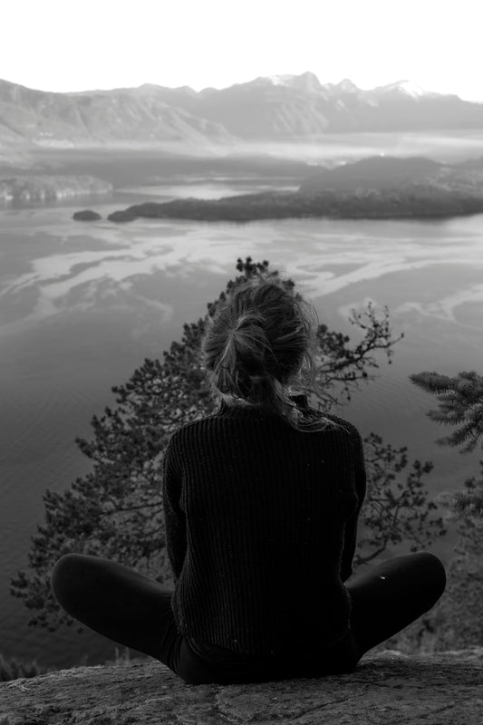 Person meditating on a mountainside overlooking a lake.
