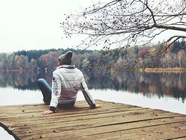Individual relaxing on a wooden dock by a tranquil lake, embracing simple self-care with nature's touch.