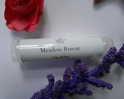 Meadow Breeze Lip Balm tube on a white surface with flowers, showcasing soothing natural care.