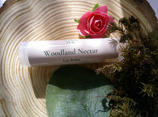 Woodland Nectar Lip Balm tube on rustic wood with flower and foliage background.