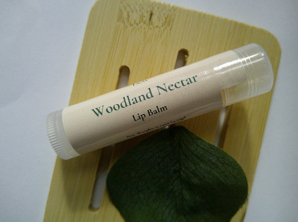 Woodland Nectar Lip Balm tube on a wooden surface with green leaf.