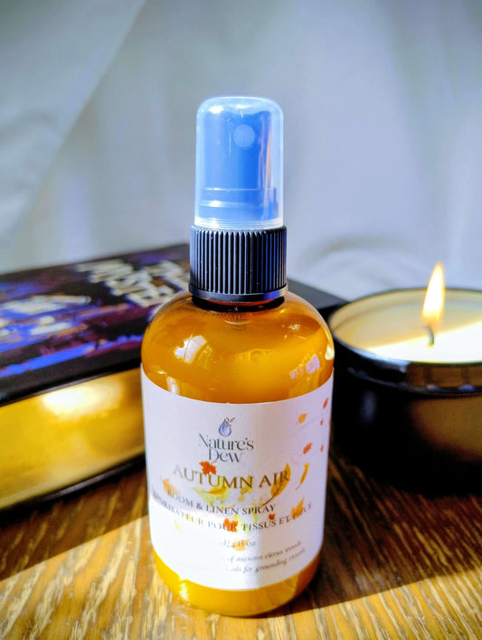 Autumn Air Room & Linen Spray bottle with citrus-wood scent near a lit candle on wooden surface