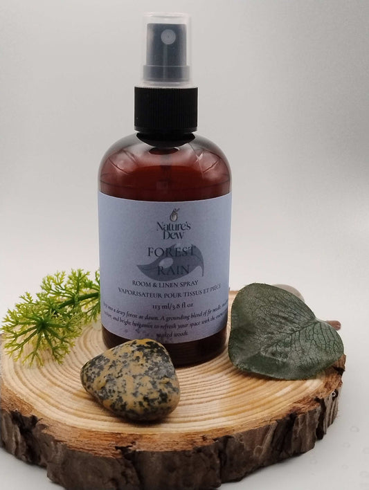 Forest Rain Room & Linen Spray on wooden slab with leaves and rocks.