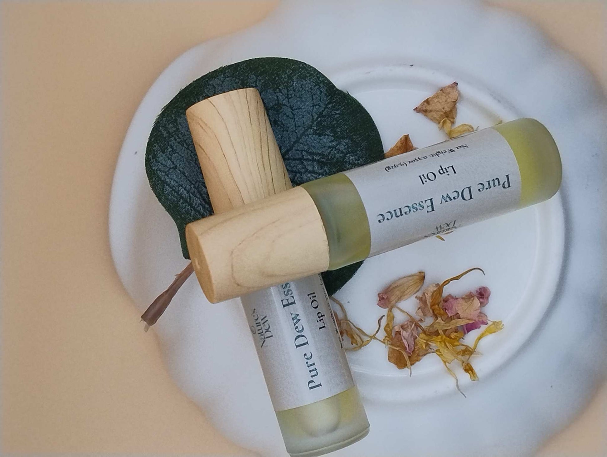 Pure Dew Essence Lip Oil bottles on a decorative plate, surrounded by leaves and petals.