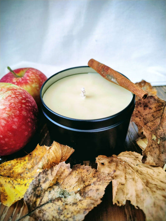 Harvested Orchard Candle with soy beeswax blend, surrounded by autumn leaves, red apples, and a cinnamon stick on wooden surface.