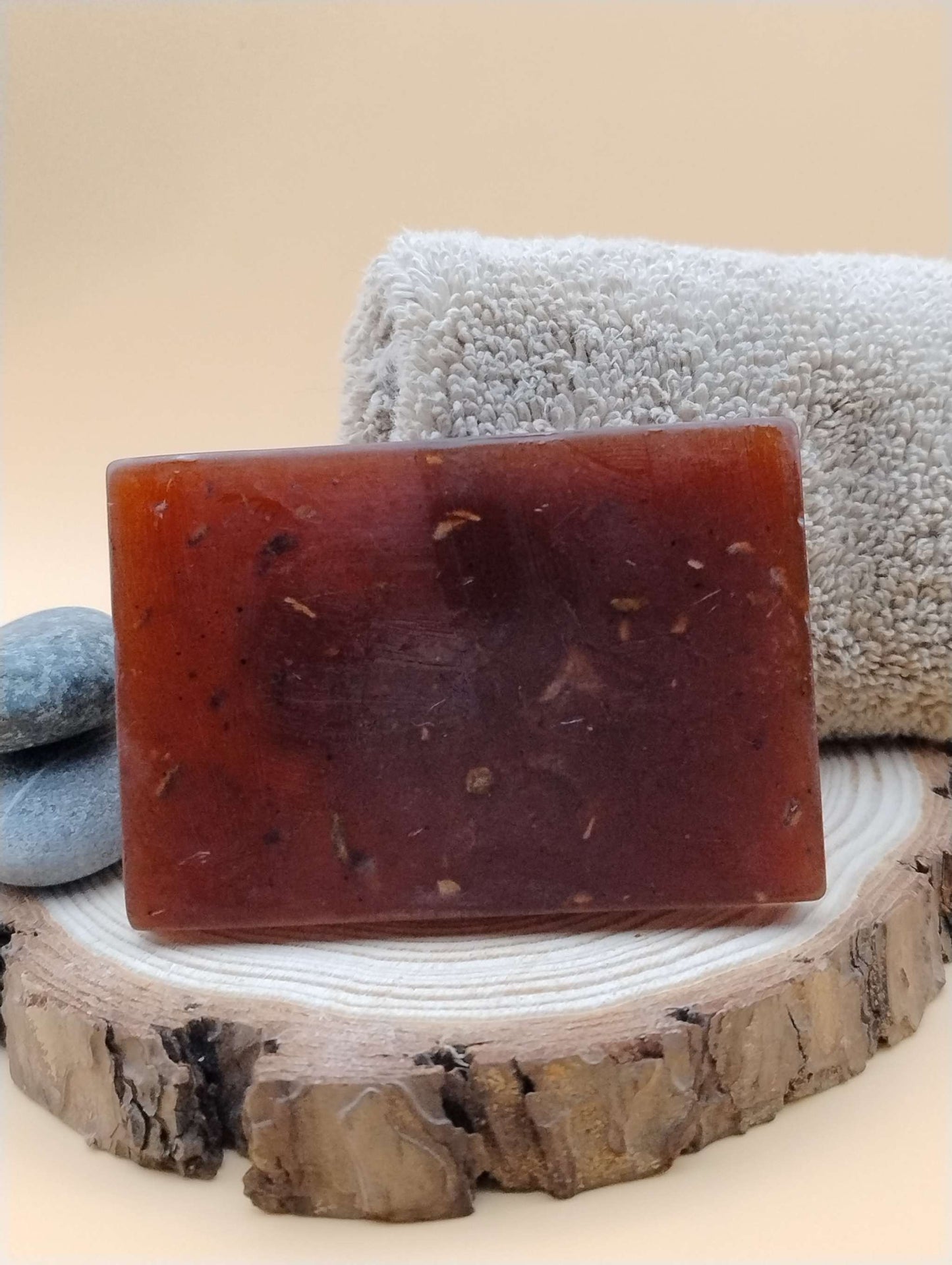 Woodland Nectar Ritual Soap Bar with earthy aroma on rustic wood slice, alongside a towel and stones.