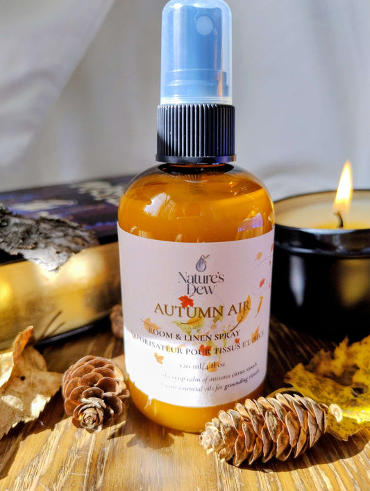 Autumn Air Room & Linen Spray with citrus and woody scent featuring bergamot, sweet orange, eucalyptus, and cedarwood in amber spray bottle near pinecones and candle