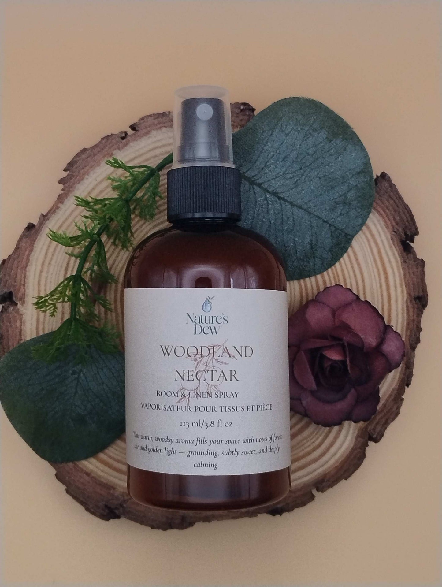 Woodland Nectar Room & Linen Spray bottle on wooden slice with leaves and flower; 113 mL natural scent.