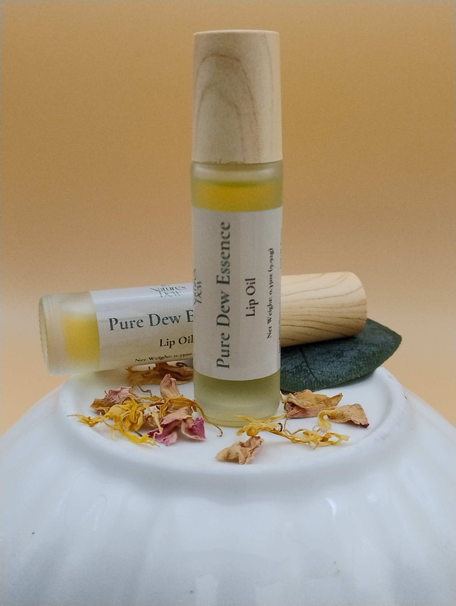 Pure Dew Essence Lip Oil with natural ingredients displayed on white ceramic surface.