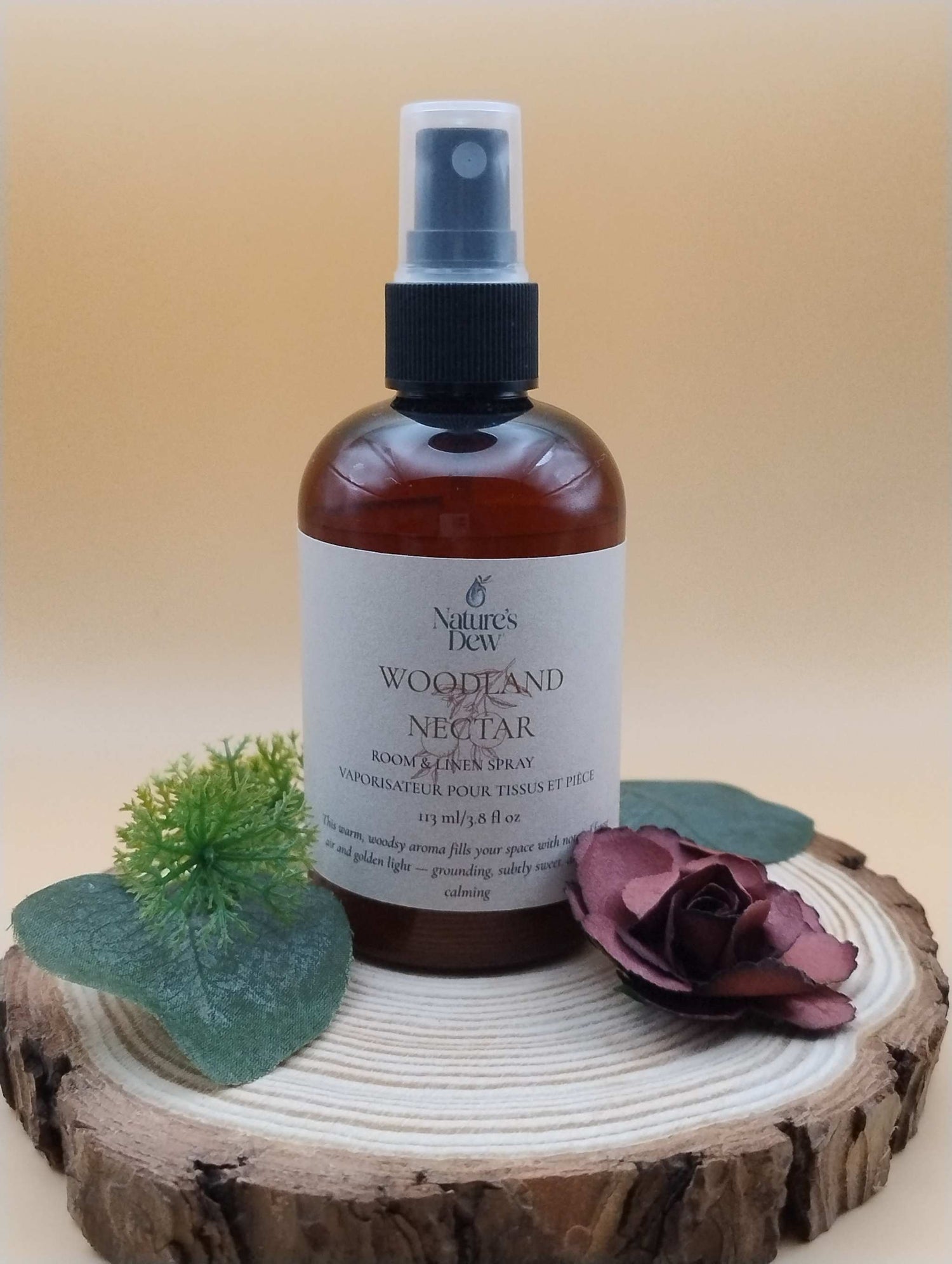 Woodland Nectar Room & Linen Spray bottle on wooden slab with greenery and rose.