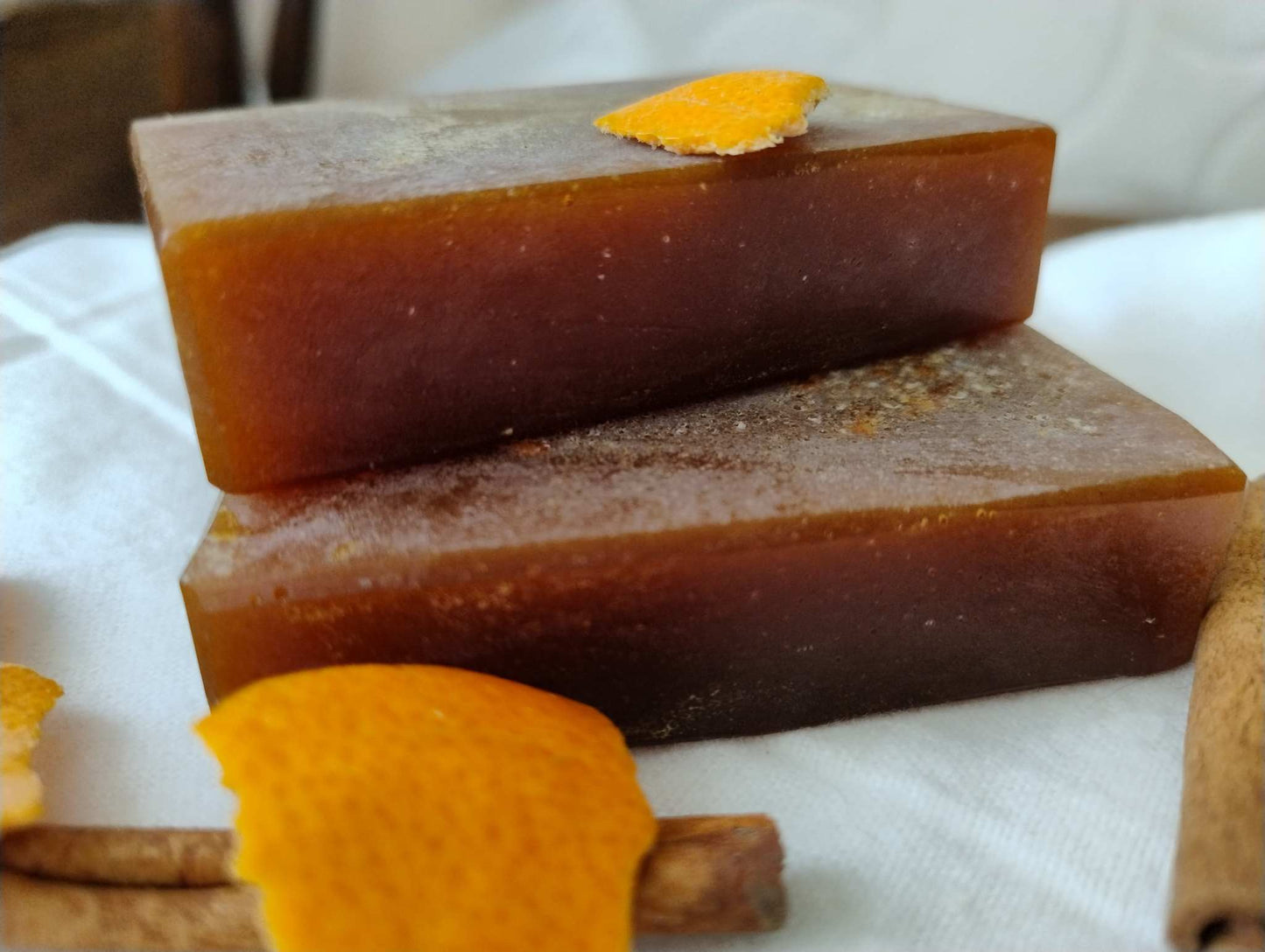 Two stacked Autumn Ember Ritual Soap bars with orange peel and cinnamon sticks on a white cloth background
